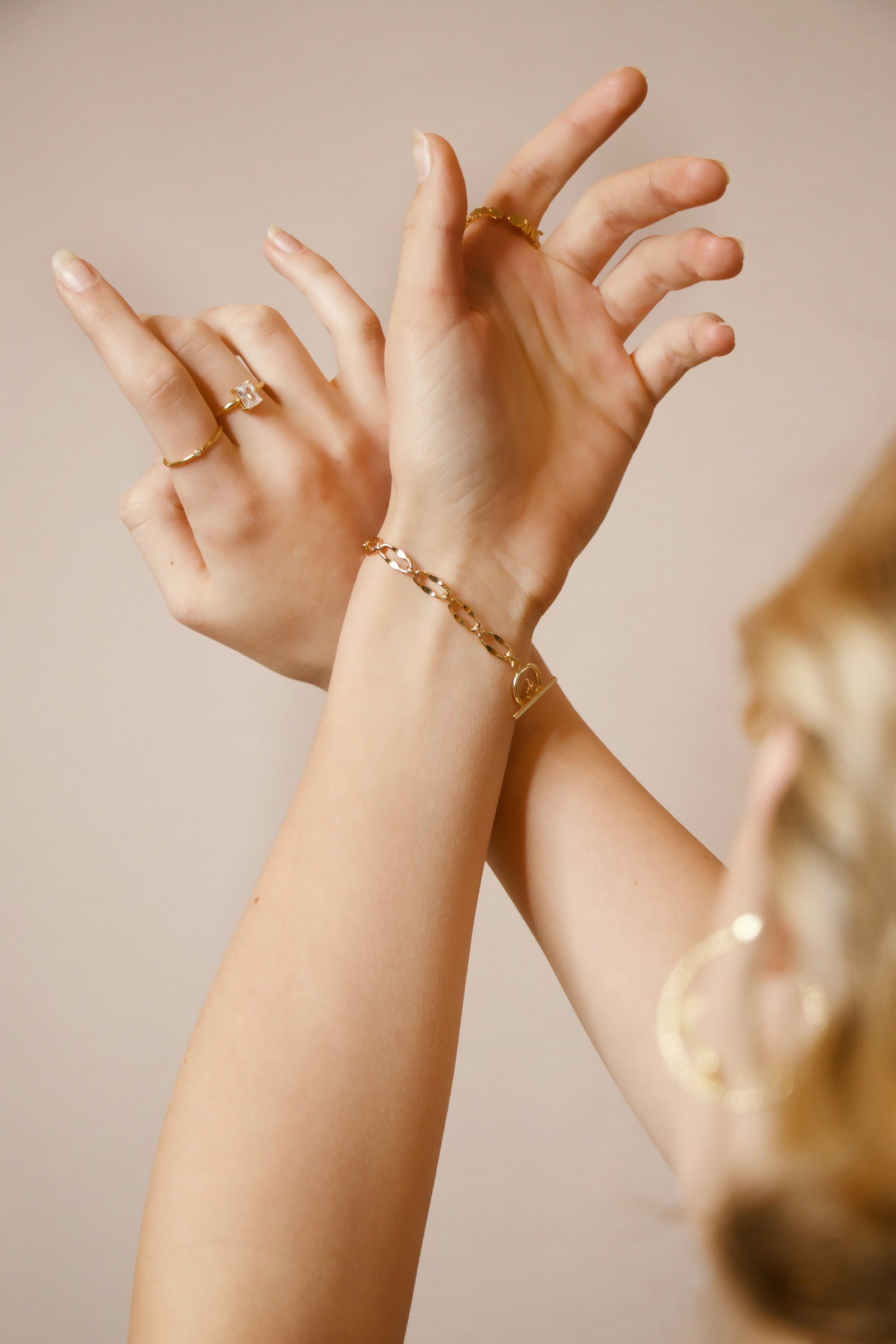Hands wearing gold rings and a delicate gold chain bracelet