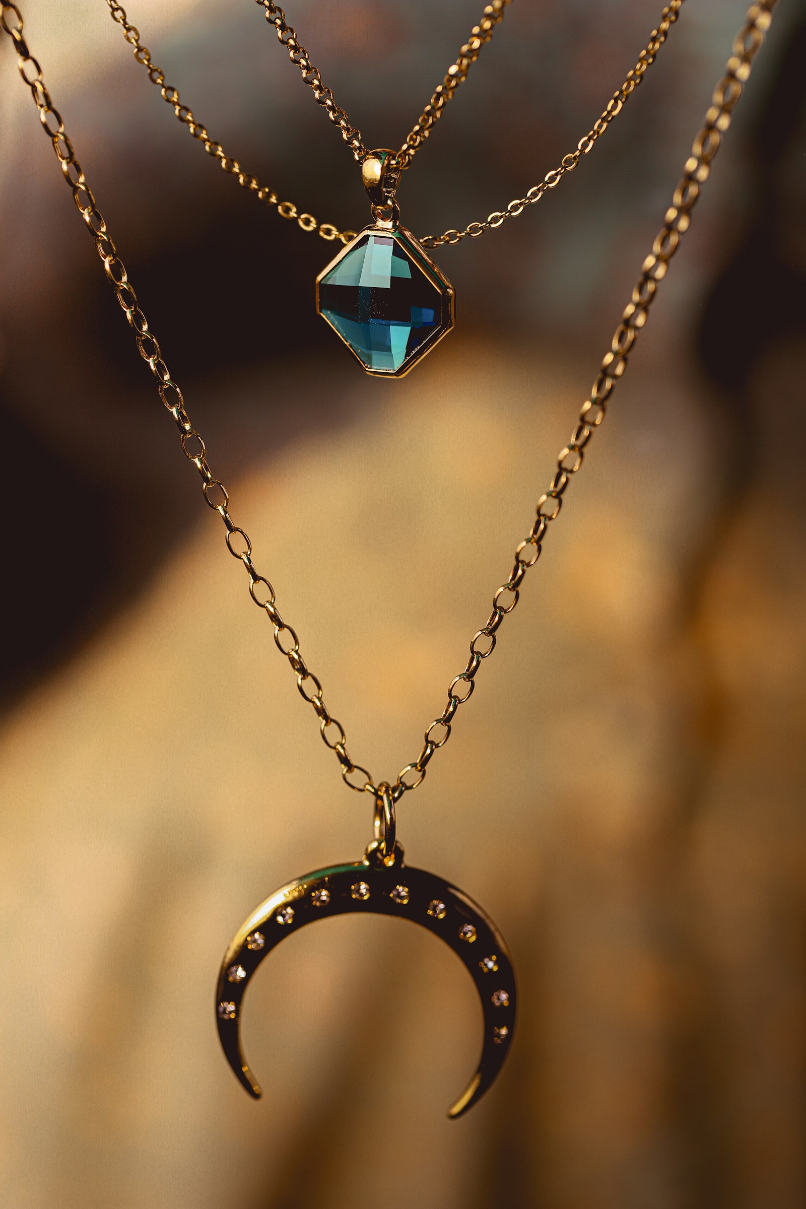 Layered gold necklaces with a crescent moon and a teal gemstone pendant