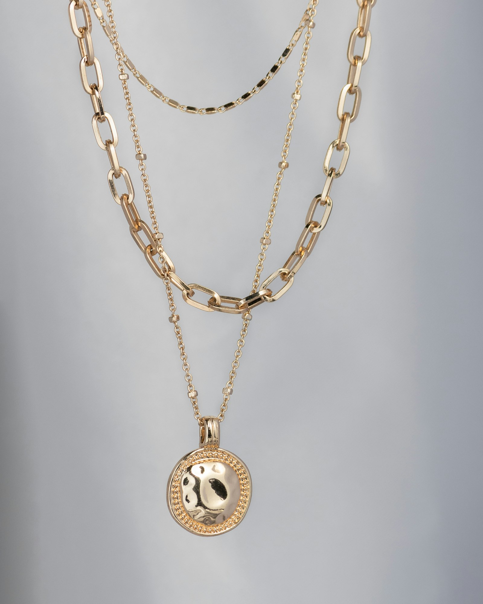 Layered gold chain necklaces with a hammered coin pendant